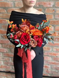 a woman wearing a black dress holding a bouquet of red, orange and yellow flowers