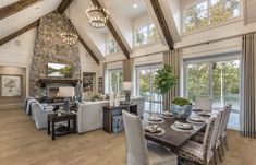 a large open concept living and dining room with wood floors, high vaulted ceilings, stone fireplace