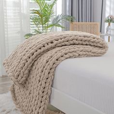 a bed with a blanket on top of it next to a chair and potted plant