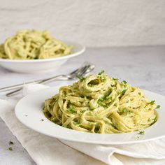 a plate of pasta with parsley on top and another bowl of pesto sauce in the background