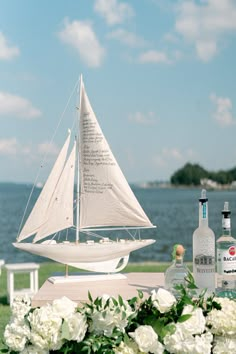 a sailboat sitting on top of a table next to white flowers and bottles of alcohol