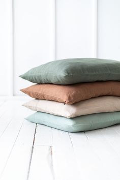 four pillows stacked on top of each other in different colors and sizes, sitting on a white wooden floor