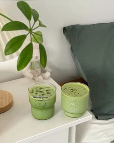 two green cups sitting on top of a white table next to a stuffed animal and pillow