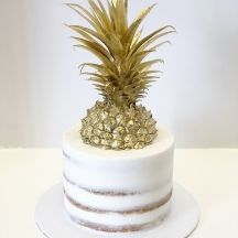 a pineapple on top of a white cake with gold decorations in the shape of stripes