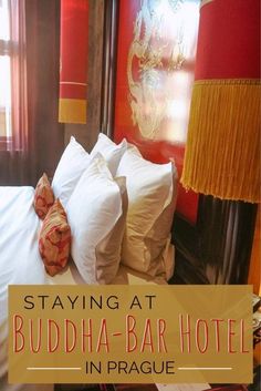 a bed with white sheets and pillows in front of a red wall that says staying at buddha - bar hotel in prague