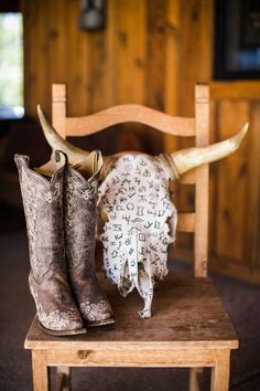 two pairs of cowboy boots sitting on top of a wooden chair next to a cow skull