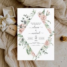 a wedding card with flowers and greenery on it next to some rings, ring boxes and other items