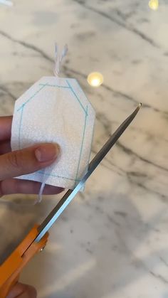 someone is cutting fabric with scissors on a marble counter top in the process of making an ornament