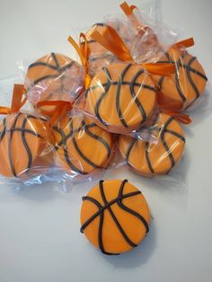 basketball cookies wrapped in plastic wrappers and tied with orange ribbons on a white table