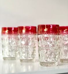 four glass cups sitting on top of a white shelf next to each other in rows