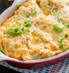 a casserole dish with green onions and cheese in it sitting on a table