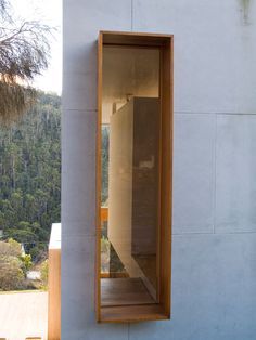 an open window on the side of a white building with trees in the back ground