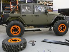 a green jeep with orange wheels parked in front of a building