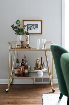 a bar cart with liquor bottles and glasses on it next to a green velvet chair