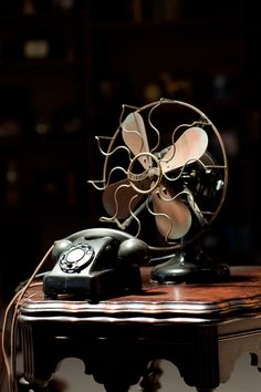 an old fashioned phone sitting on top of a wooden table next to a small fan