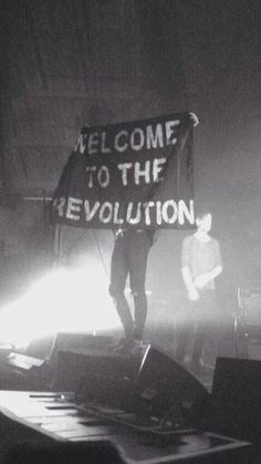 a man standing on top of a stage holding a sign that reads welcome to the revolution