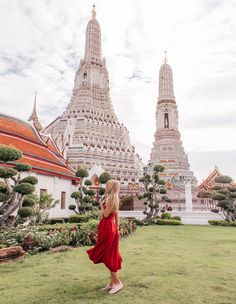 a woman in a red dress is walking near the grand palace and watra that has many spires