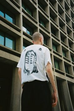 a man standing in front of a building wearing a t - shirt with a woman's face on it