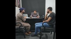 three men sitting at a desk in an office