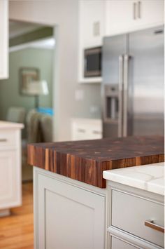 a kitchen with white cabinets and wood counter tops in the foreground is a stainless steel refrigerator