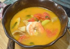 a bowl of soup with shrimp, carrots and celery on a wooden table