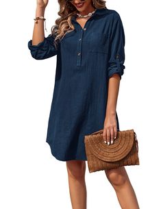 a woman in a blue shirt dress holding a brown purse and posing for the camera