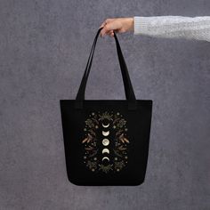 "The black canvas tote bag features all over printed design with beautiful moon phases and winter foliages illustration! The design comes from my original illustration \"Moonlight Garden - Winter Brown\". A spacious and trendy tote bag to help you carry around everything that matters. * 100% spun polyester fabric * Bag size: 15″ × 15″ (38.1 × 38.1 cm) * Capacity: 2.6 US gal (10 l) * Maximum weight limit: 44lbs (20 kg) * Dual handles made from 100% natural cotton bull denim * Handle length 11.8″ (30 cm), width 1″ (2.5 cm) * The handles can slightly differ depending on the fulfillment location * Blank product components sourced from China This product is made especially for you as soon as you place an order, which is why it takes us a bit longer to deliver it to you. Making products on deman Black Bohemian Canvas Bag For Daily Use, Moonlight Garden, Garden Winter, Boho Tote Bag, Boho Tote, Magical Winter, Brown Tote Bag, Trendy Tote Bags, Tote Bag Black