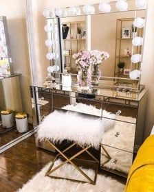 a vanity with a mirror, stool and flowers on it in front of a yellow couch