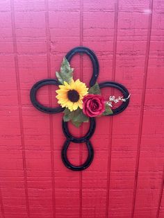 a cross made out of black metal with flowers on the front and back sides, hanging from a red door