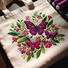 a white bag with pink flowers and butterflies on it sitting on a table next to some crayons