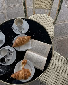 two croissants and an open book sit on a table with coffee cups