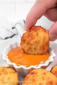 a person dipping some food into a small white bowl with sauce on the side and another hand reaching for it