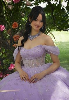 a woman in a purple dress sitting on the ground next to some flowers and trees