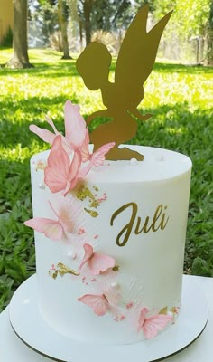 a white cake with pink flowers on it and a gold fairy topper that says julia