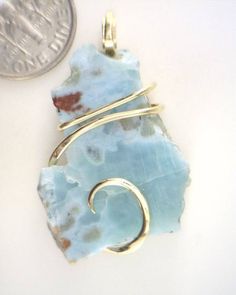 31.61ct Larimar Freeform Shard in 14kt Gold Wire Wrap Pendant 31.61 carats total weight Check Out Our Other Auctions and Ebay Store! Total weight 31.61 carats including wrap Size 37 mm by 22 mm by 7 mm including wrap     Up for sale is a beautiful rare polished Larimar piece in a hand forged 14kt gold art wire wrap. This gorgeous stone is polished to a high sheen on the front. It has a fascinating blend of bright whites and brilliant blues. To top it all off are the swirling waves of glowing 14kt gold securely gripping the stone and really making it pop. Truly a perfect piece and it could be yours!!   Larimar is a new and rare gemstone that has been found in only one location: in a mountainous, relatively inaccessible region of the Dominican Republic overlooking the Caribbean Sea. This gem Sea Glass Wire Wrapping, Unique Untreated Yellow Gold Jewelry, Unique Untreated 14k Gold Jewelry, Elegant Larimar Pendant Jewelry, Elegant Handmade Larimar Jewelry, Luxury Untreated Jewelry For Gift, Luxury Untreated Jewelry As A Gift, Aquamarine Gemstone Jewelry In Yellow Gold, Yellow Gold Aquamarine Pendant Jewelry