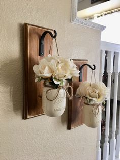 two mason jars with flowers are hanging on the wall