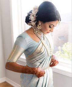 a woman in a white and blue sari is holding her hands together while looking out the window