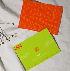 two orange and green business cards sitting on top of a white sheet with black writing