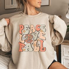 This trendy, retro style Fall Sweatshirt feature the saying Peace, Love, Fall and a cute 70s vibe. Comes in multiple colors! Find more styles here: www.etsy.com/shop/jadeandroseshop ❤️ Please note that for the oversized look you need to buy 1-3 sizes larger than you normally wear. If you prefer the standard Unisex fit order your typical size. For women, if you prefer a more women's fit sweatshirt please size down 1 size, as this sweatshirt is a Unisex fit ❤️ This unisex heavy blend crewneck swea Cheap Heather Grey Sweatshirt For Fall, Trendy Long Sleeve T-shirt With Lettering, Retro Long Sleeve Tops With Letter Print, Retro Graphic Print Tops For Fall, Retro White Tops With Lettering, Vintage Screen Print Tops For Fall, Vintage Screen Printed Tops For Fall, Casual Retro Print Tops For Fall, Retro Relaxed Fit Tops With Lettering