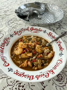 a white bowl filled with soup next to a silver serving dish on a lace tablecloth