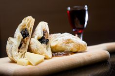 two pastries on a wooden cutting board next to a glass of wine and cheese