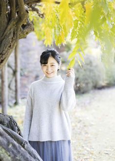 a woman standing under a tree holding onto leaves