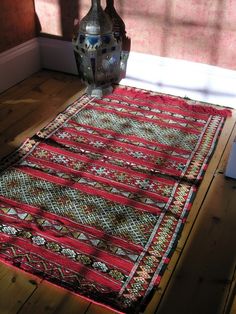 a vase sitting on top of a wooden floor next to a red and green rug