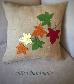 an embroidered pillow with leaves on it sitting on a couch next to a white chair