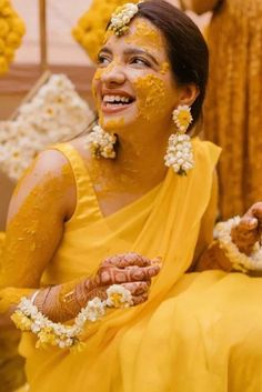 a woman with yellow paint on her face and flowers in her hair, sitting down