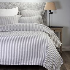 a bed with white and blue striped comforter next to a lamp on a nightstand