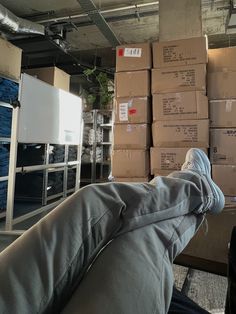 someone is laying on the couch with their feet up in front of cardboard boxes stacked on top of each other