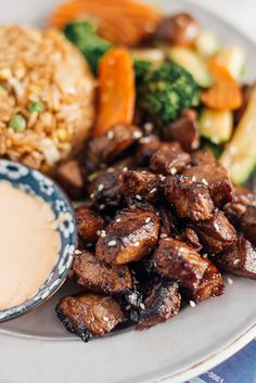 a white plate topped with meat and veggies next to a bowl of sauce