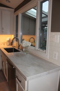 a kitchen with white cabinets and marble counter tops in front of a large open window