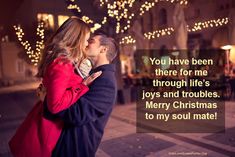 a man and woman kissing on the street with christmas lights in the backgroud